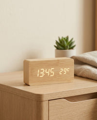 Wooden LED digital alarm clock on a bedside table showing the time and temperature